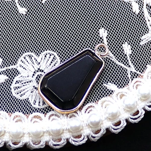 Dettaglio macro di un ciondolo in pietra naturale nera trapezoidale con bordo dorato