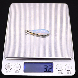 Opal teardrop pendant with silver-plated edge being weighed at 3.2 grams on a scale