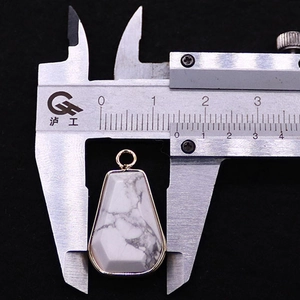 Ciondolo in turchese bianco trapezoidale con bordo dorato misurato su un calibro di 1,5 cm
