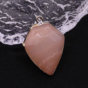 Macro detail of a rose quartz shield pendant with faceted cut and gold plated metal edge