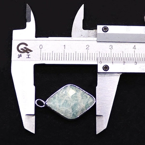 Caliper measuring a faceted blue stone pendant with silver metal frame and jump ring