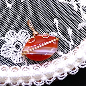 Detailed close-up of wire-wrapped oval red striped agate pendant on white lace