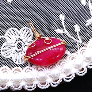Macro detail of wire-wrapped red striped agate oval pendant with golden metal craft work