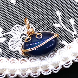 Detail of handmade gold wire-wrapped oval striped agate pendant on vintage lace background