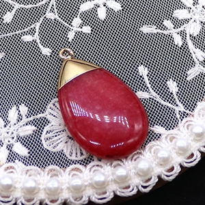 Detail view of teardrop red agate stone pendant with gold clasp on lace and pearl background