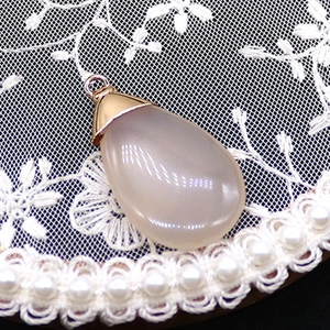 Detail shot of a white water drop stone pendant with gold clasp on white lace and pearls