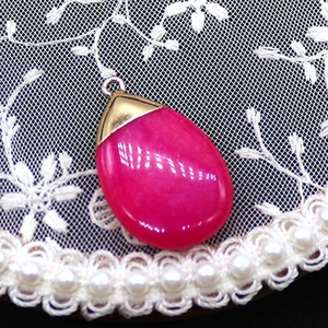 Close-up of rose red teardrop stone pendant with gold clasp on white lace background