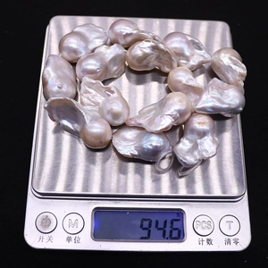 Gros plan de 94,6g de perles d'eau douce baroques avec lustre arc-en-ciel sur balance