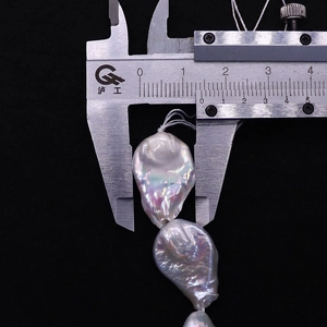 Macro shot of measuring a 14-15mm baroque freshwater pearl with a caliper on black