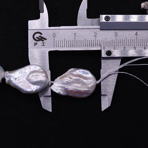 Macro detail of a 25mm white baroque pearl being measured with a digital caliper