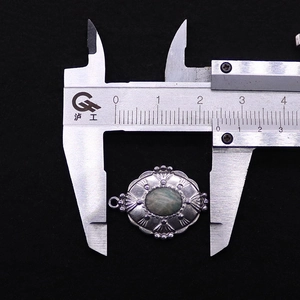 Detail eines ovalen Vintage-Anhängers aus Edelstahl mit grünem Stein und Maßangabe