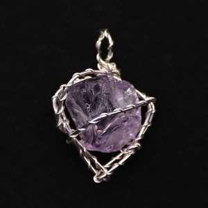 Makroaufnahme von Amethyst-Rohstein-Anhänger mit silberner Drahtwicklung auf schwarzem Samt