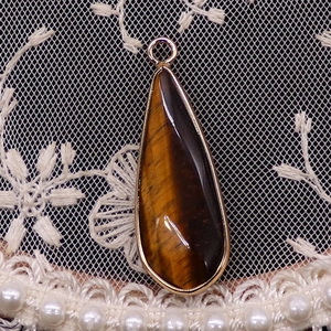 Détail d'un pendentif en œil de tigre en forme de goutte avec bordure dorée sur dentelle