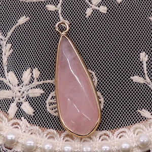 Détail d'un pendentif goutte en quartz rose facetté avec bordure en métal doré