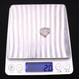 Macro-opname van een 2,0g rozenkwarts hart hanger met goudkleurige rand op een weegschaal
