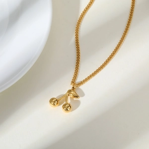 Détail du collier cerise doré avec perles polies et chaîne à maillons fins sur fond blanc