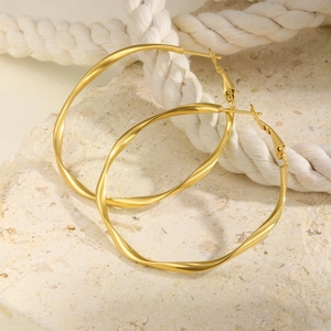 Macro detail of gold Mobius hoop earrings with twisted texture on a stone background