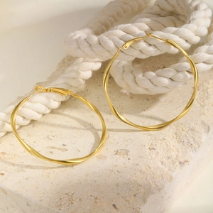 Detail of gold twisted Mobius hoop earrings resting on stone and woven rope background