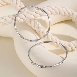 Polished silver stainless steel Mobius twist hoop earrings on a minimalist white prop
