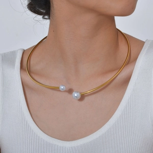 Dettaglio di un girocollo minimalista in metallo dorato con due perle indossato da una modella