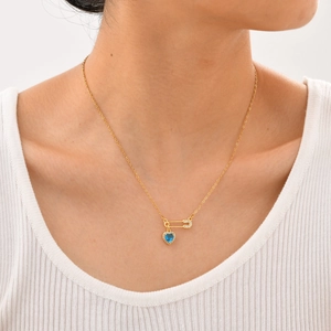 Détail du collier doré avec pendentif épingle à nourrice et zircon bleu en cœur