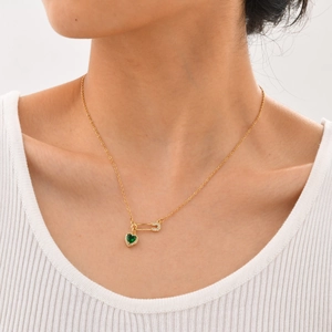 Gros plan d'un collier doré avec pendentif cœur vert et épingle ornée de zircons