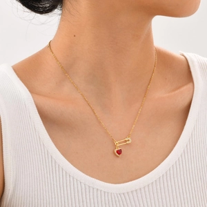 Gros plan d'un collier épingle à nourrice doré avec zircon coeur rouge sur un mannequin