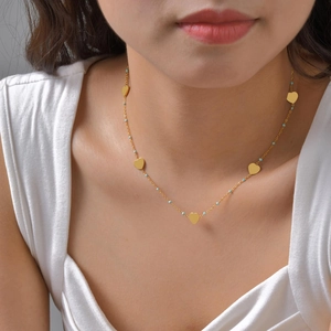 Collier cœur en acier doré avec perles bleues porté sur un cou de femme