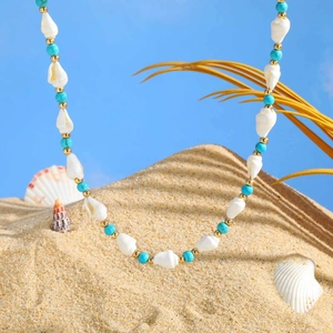 Detaillierte Strandkette mit türkisen Perlen, Muscheln und Goldperlen auf dem Sand