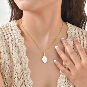 Detail of gold stainless steel necklace featuring a white shell oval letter A pendant