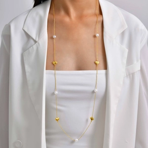 Détail d'un long collier pull doré avec perles blanches et pendentifs coeurs sur mannequin