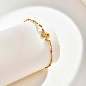 Detail of golden snake charm bracelet with colorful beads on white display stand