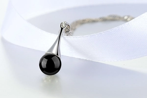 Macro di un ciondolo a goccia in argento con perla di onice nera su seta bianca