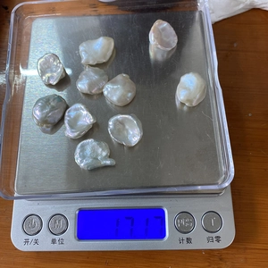 Close-up of ten irregular white baroque pearls being weighed on a digital scale
