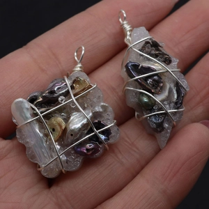 Handcrafted wire-wrapped shell and pearl pendants held by a hand on a black background