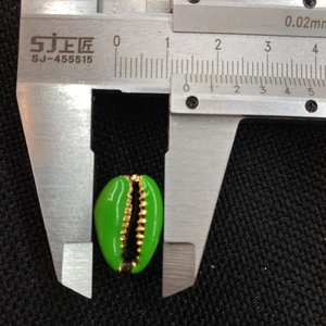 Detailed measurement of green shell charm with golden trim using a digital caliper