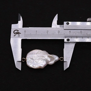 Macro view of natural baroque pearl connector with gold rings measured by caliper