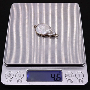 Detailed macro view showing a 4.6g baroque pearl pendant with gold frame on a scale
