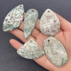 Primo piano di ciondoli assortiti in agata verde naturale tenuti in mano per gioielli