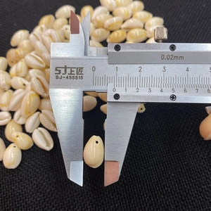 Macro detail of a natural beige seashell being measured with a metal caliper for DIY jewelry