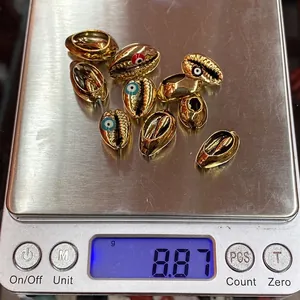 Vue détaillée de perles coquillage dorées avec motifs œil protecteur sur une balance de précision