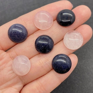Polished 15mm round rose quartz and blue sandstone cabochons held by hand for DIY jewelry