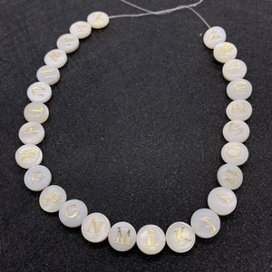 Macro shot of mother of pearl alphabet beads with golden engraved letters A to Z