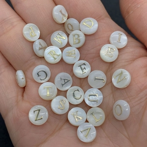 Macro detail of mother-of-pearl flat round beads with gold letters for jewelry making