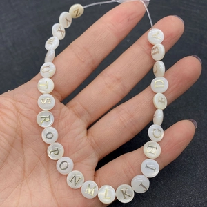Close-up of round flat shell beads with gold engraved A-Z alphabet letters