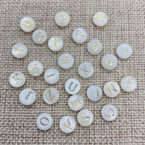 Macro shot of natural white shell beads with golden engraved letters on burlap texture