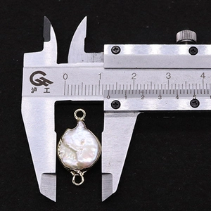 Détail d'un pendentif perle baroque avec bordure dorée mesuré au pied à coulisse
