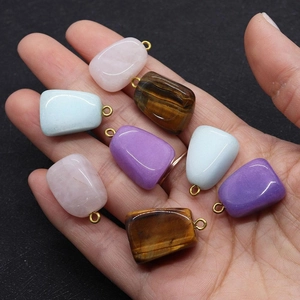 Macro view of irregular Tiger Eye and Rose Quartz pendants with gold metal ring held in hand
