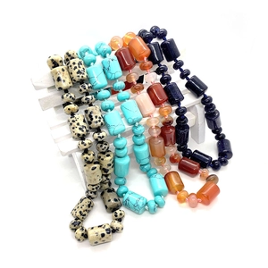 Assorted cylindrical natural stone necklaces featuring rose quartz and agate on a bench