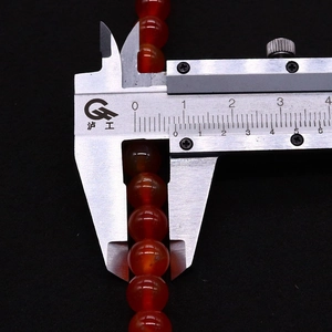 Misurazione macro di una perlina in pietra naturale rossa da 8mm con calibro in metallo